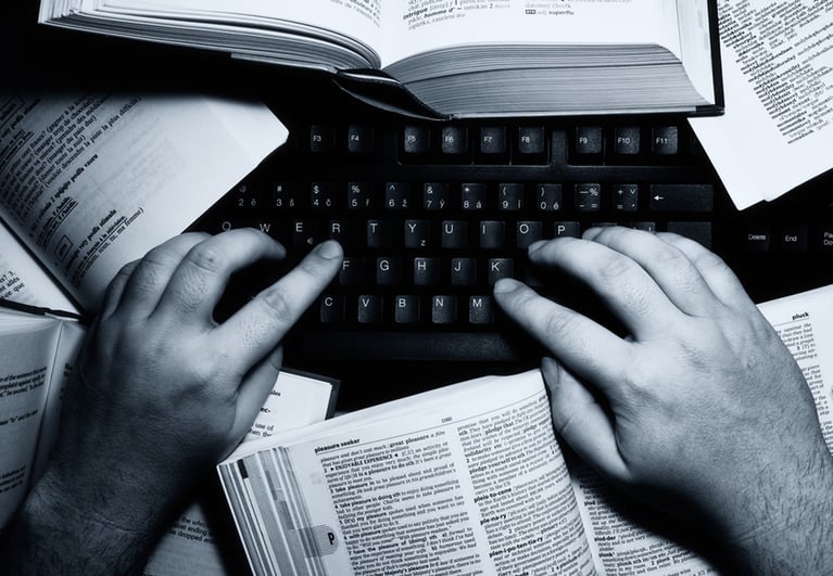 man typing on keyboard with books next to him